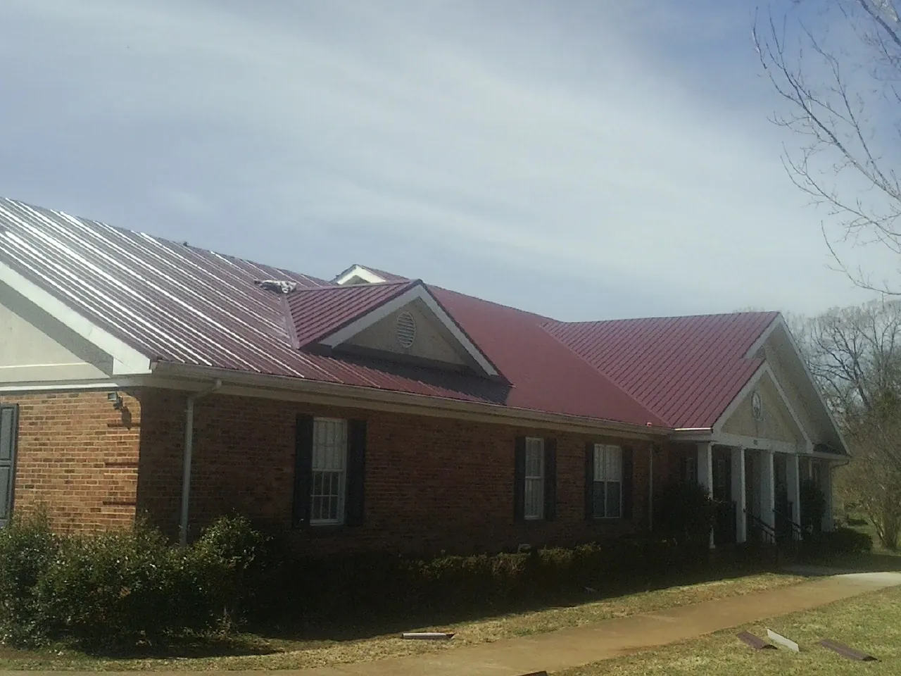Red metal roof with gabled entries on a long brick building, from a Hail Damage Roof Repair job in Kauneonga Lake