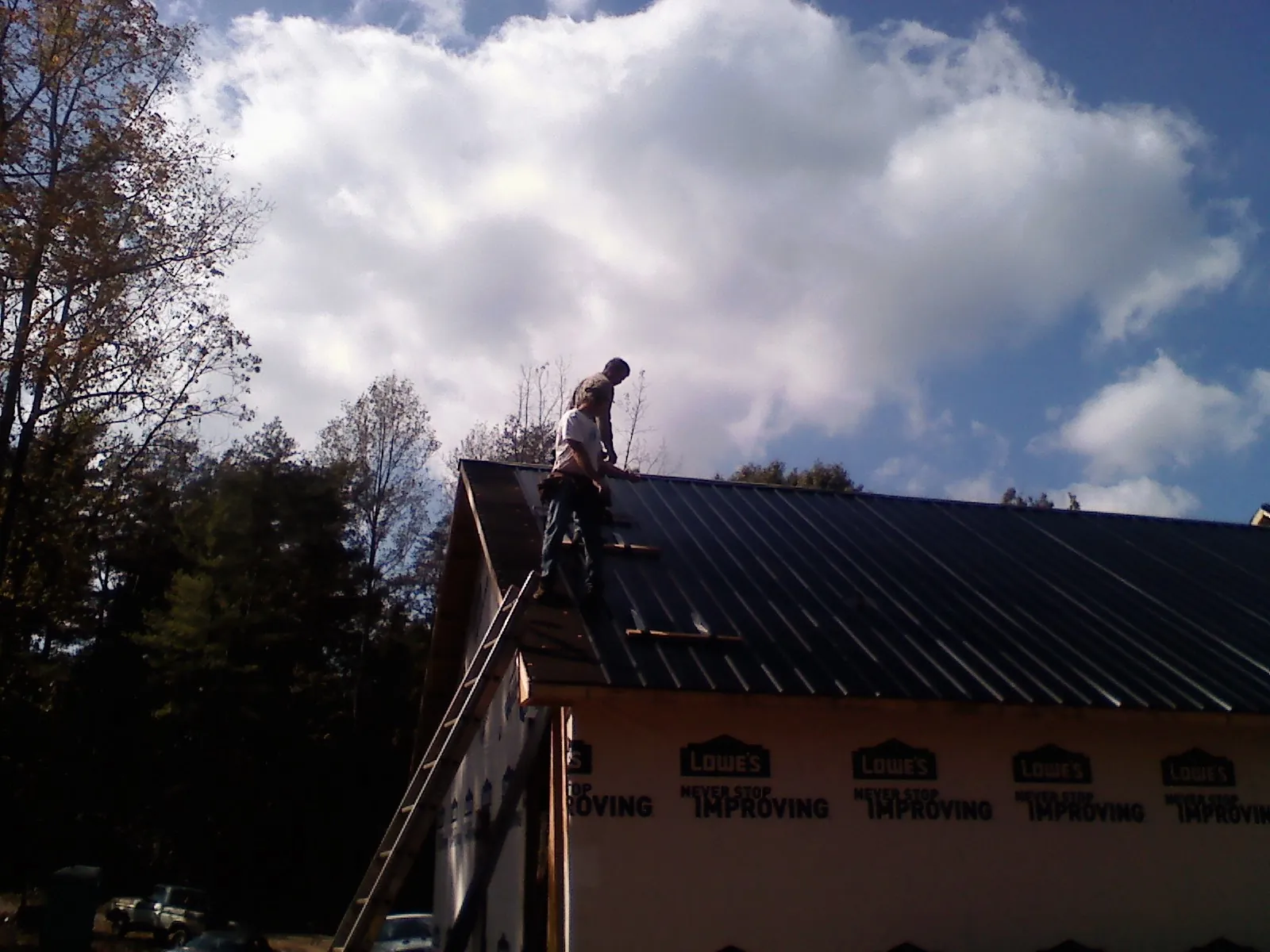 Roofer fastening dark metal panels high against a cloudy sky, from a Roof Inspection job in Kauneonga Lake