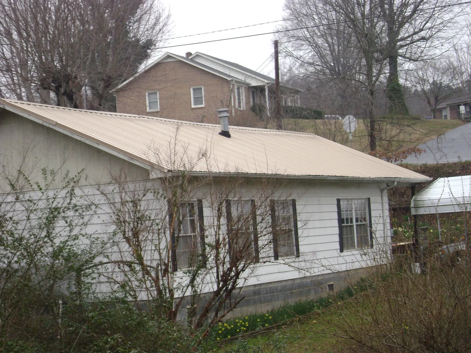 Tan metal roof on a white sided house set into a hillside — Commercial Roofing by Roofing Brothers in Kauneonga Lake