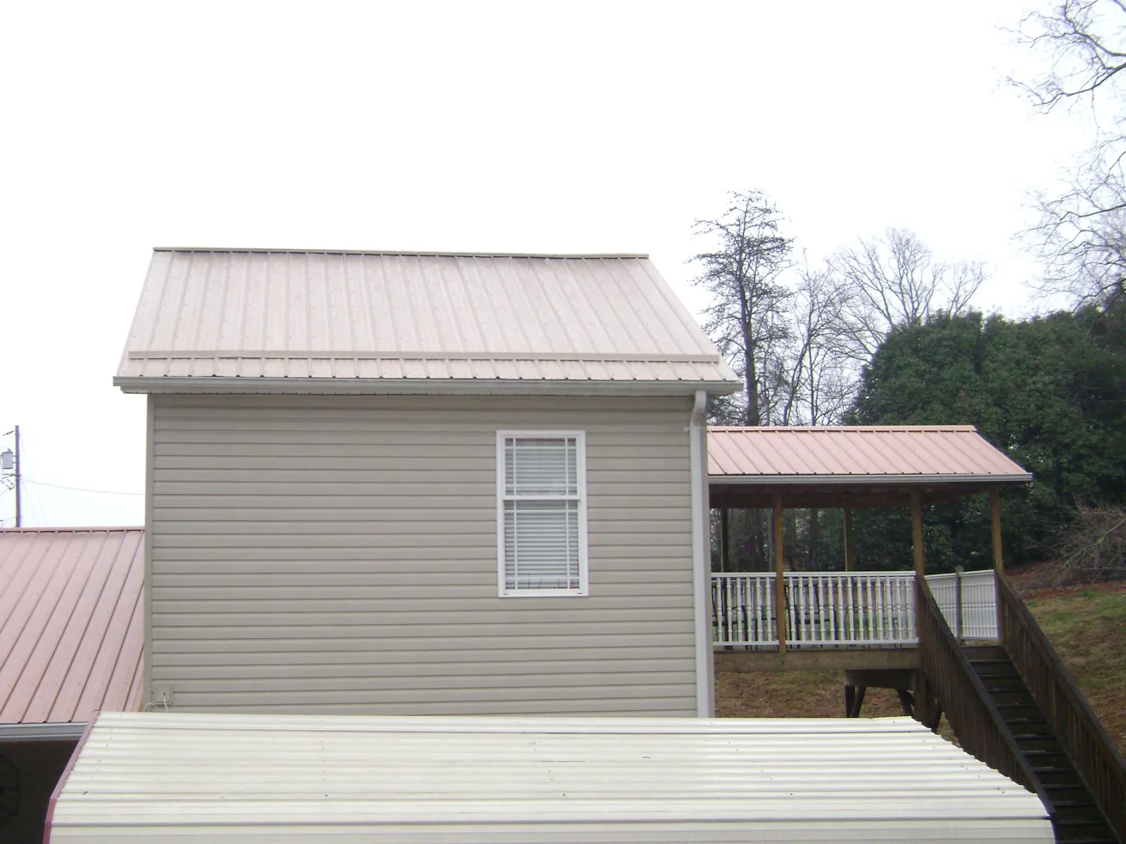 Tan metal roofs on a two story addition and attached porch, from a Roof Replacement job in Kauneonga Lake